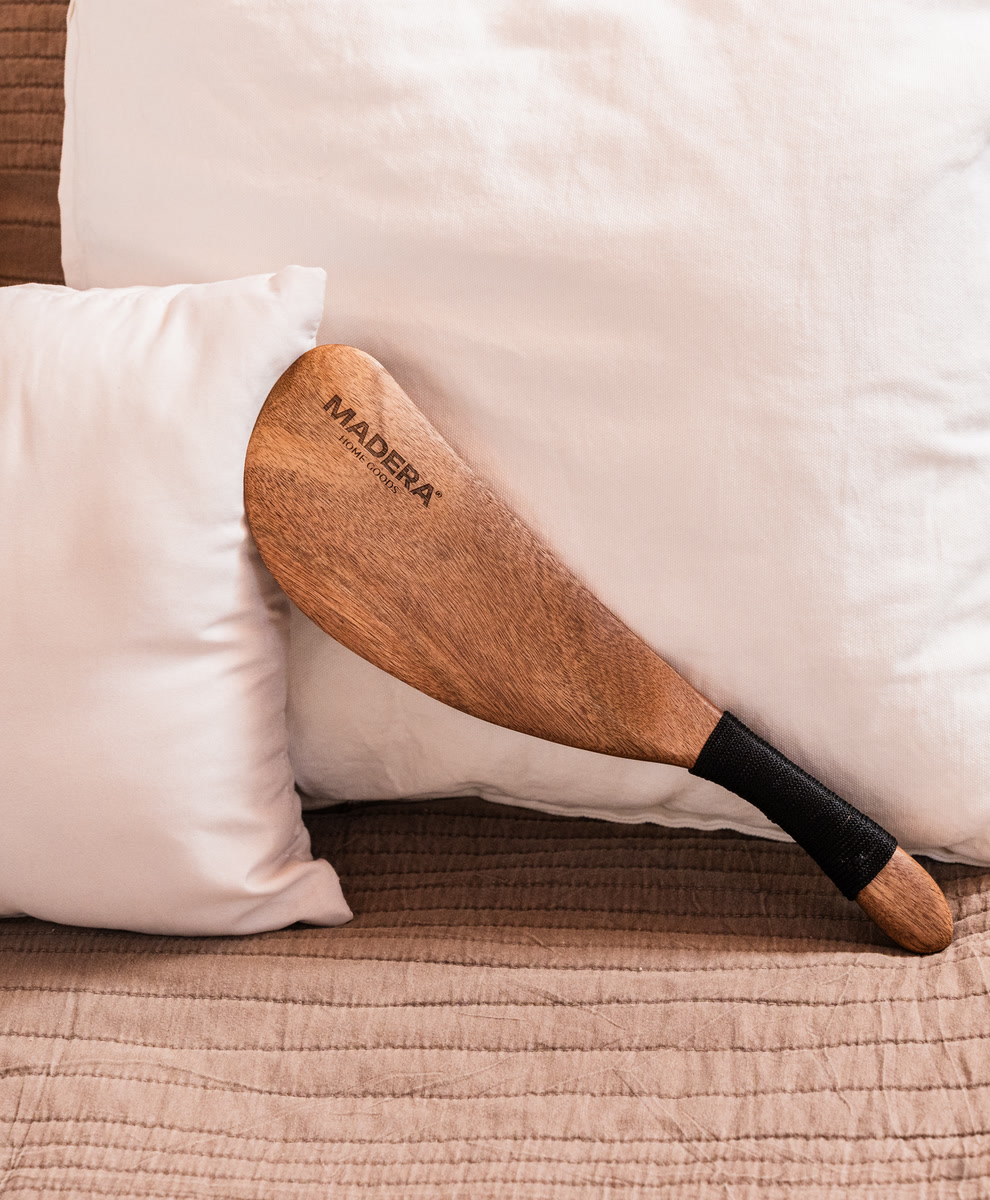 The Madera acacia wood bed sheet tucker leaning on white pillows on a made bed