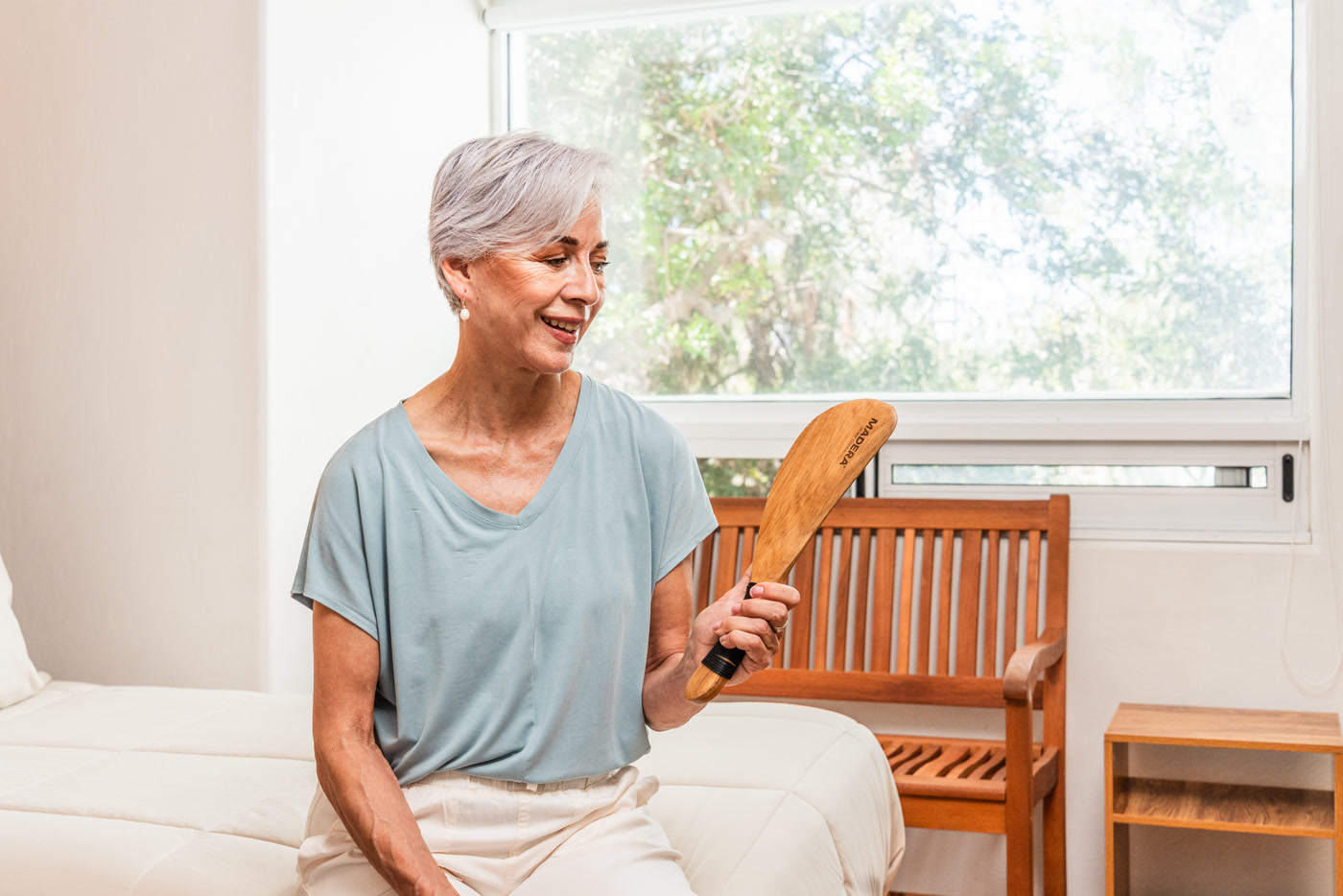 A smiling older woman sitting on a bed, holding the Madera tucker